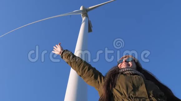 能源生产微笑的女孩正在享受乐趣在风力涡轮机的特写下挥动手臂对抗天空视频的预览图