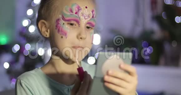 一个有着节日妆容的迷人女孩看着一面小镜子用口红涂上嘴唇视频的预览图