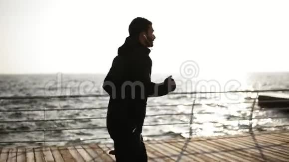 在靠近海边的码头上奔跑或慢跑的年轻男子的侧视镜头户外录像视频的预览图