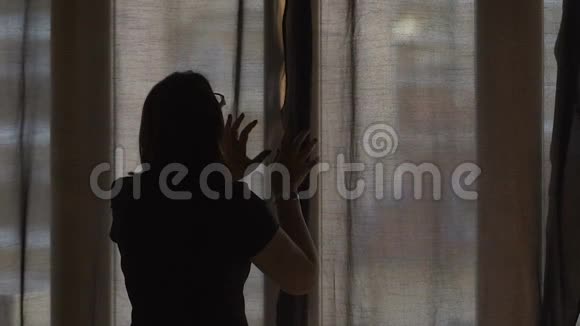 女人拉开黑暗的窗帘让温暖的夏天阳光在她舒适的家慢镜头视频的预览图