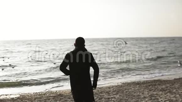 年轻的运动男性白种人身穿黑色运动服带着耳机在海滨跑步视频的预览图