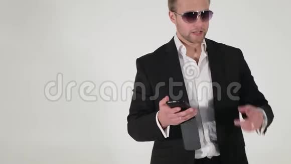穿西装戴太阳镜的帅哥手里拿着智能手机说话视频的预览图