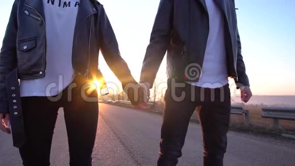 一对相爱的夫妇穿着皮夹克站在黎明的路中间手牵手视频的预览图
