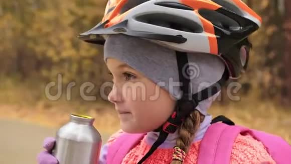 孩子喝铝瓶里的水一个高加索儿童在秋季公园骑自行车小女孩穿黑衣服视频的预览图