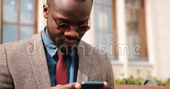 年轻的非裔美国人坐在长凳上用他的智能手机打字商业和生活方式概念视频的预览图