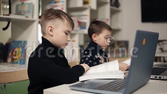 两个小男孩坐在教室里的笔记本电脑前看书教育过程视频的预览图
