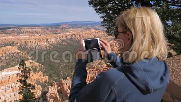 站在布莱斯峡谷眺望点的女游客和智能手机的照片视频的预览图