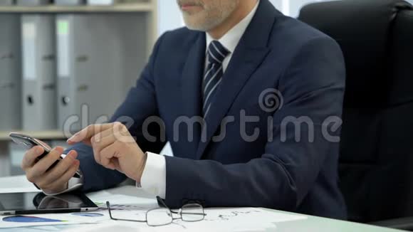 深色西装男士用平板电脑和眼镜在桌旁拨打电话和交谈视频的预览图