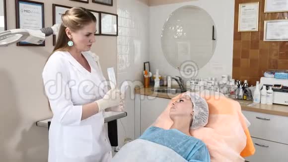 保健诊所的美容师与一位女性客户交谈解释面部手术的细节并显示无菌视频的预览图