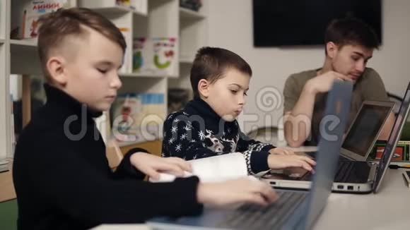 两个小男孩在笔记本电脑键盘上打字而他们的男程序员老师正坐在附近视频的预览图