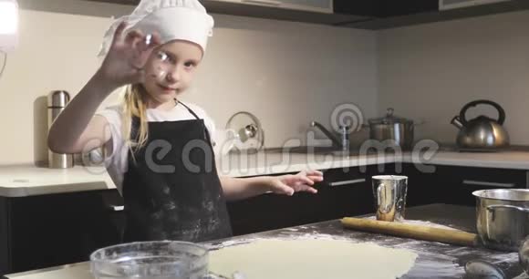 穿着围裙和厨师帽的可爱女孩在饼干面团上切出形状视频的预览图