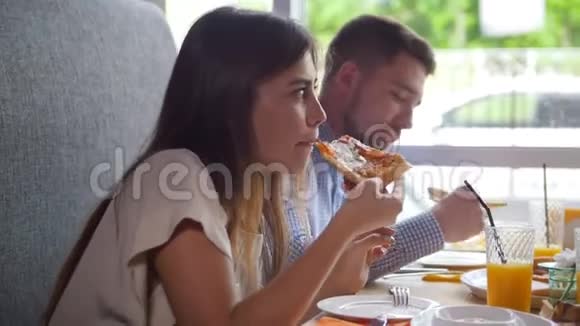 四个年轻的朋友坐在咖啡馆里吃早餐披萨果汁甜点视频的预览图
