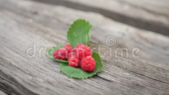 成熟的红色覆盆子放在绿色叶子的木桌上视频的预览图