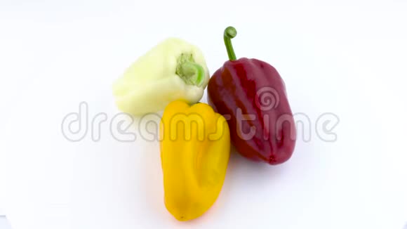 从上面可以看到三个甜辣椒白色黄色和红色在转盘上旋转孤立于白色之上视频的预览图