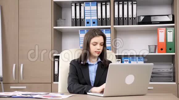 女商人在笔记本电脑上打字然后转向相机微笑视频的预览图
