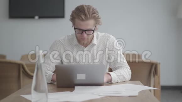 一位思想深邃的商人戴着眼镜坐在一间舒适的办公室里坐在上网本前的桌子旁视频的预览图