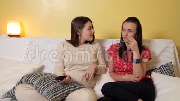 两个年轻女孩坐在家里的沙发上下雨天看电视聊天家雨友谊视频的预览图