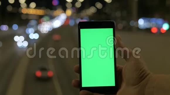 一个男人手拿着一个绿色屏幕的智能手机背景是运动模糊的汽车灯视频的预览图