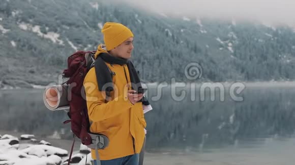 美国旅行者在徒步冬季旅行中使用智能手机白雪皑皑的湖面和背景下的群山旅行和视频的预览图