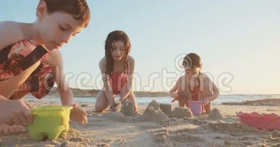 三个孩子在日落时在海滩上建造沙堡视频的预览图