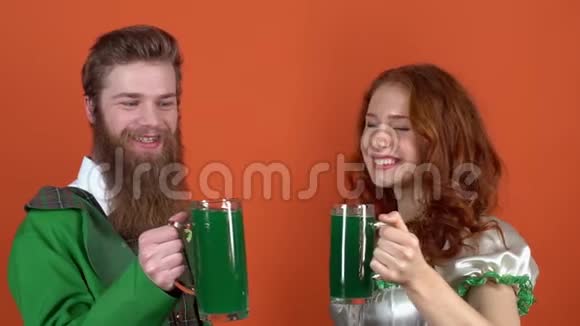 身着盛装庆祝圣帕特里克节的年轻一对夫妇橙色的墙上隔离了一天为绿色的啤酒干杯视频的预览图
