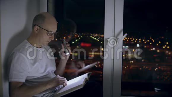 成年人坐在窗台上在黑暗中用手电筒浏览书页视频的预览图