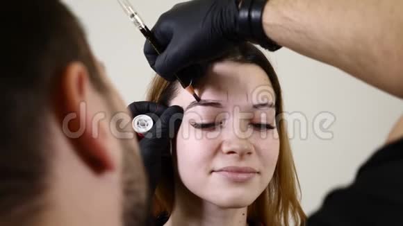 美容院男性美容师戴黑色手套在女性眉毛上做永久化妆程序年轻女子微笑视频的预览图