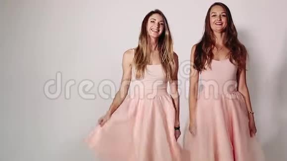 前面看到两个迷人的时尚的女孩挥舞着他们张开的裙子跳舞和跳跃可爱的女孩视频的预览图
