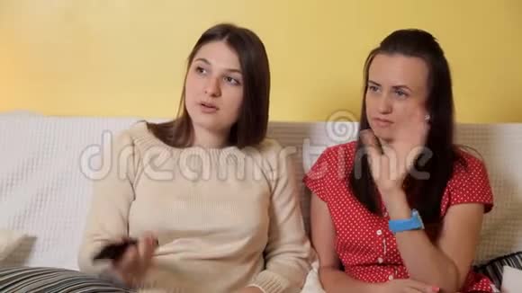 两个年轻女孩坐在家里的沙发上下雨天看电视聊天家雨友谊视频的预览图