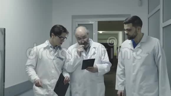 三位男医生在医院走廊散步时讨论一位病人笔记4K视频的预览图