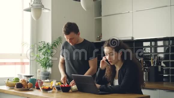 一对严肃的白种人在厨房里的好夫妇男人正在切沙拉他站着沉默女人坐在桌子上工作视频的预览图