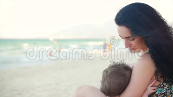 妈妈带着孩子坐在海边享受新鲜空气妈妈在给孩子喂奶逗他开心视频的预览图