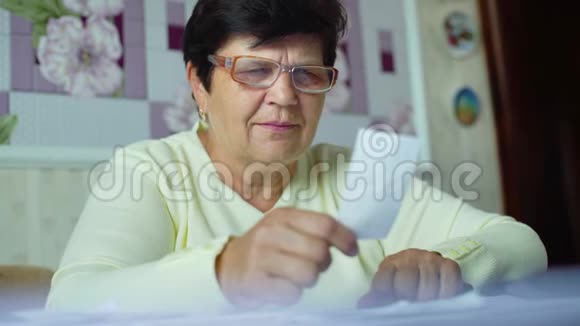 老年妇女在眼镜中的注意力不集中检查家里的日常开支视频的预览图