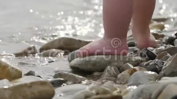 小婴儿的孩子的腿和脚趾在海边散步成小波浪海滩上的卵石海浪视频的预览图