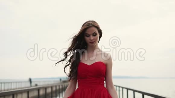快乐的女人穿着漂亮的红色长裙走过码头视频的预览图