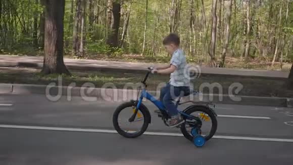 小男孩骑自行车沿着城市公园骑蓝色自行车的小型自行车视频的预览图