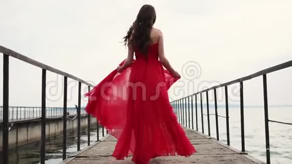 无忧无虑的微笑的女人走过码头挥舞着她的丝红色连衣裙视频的预览图