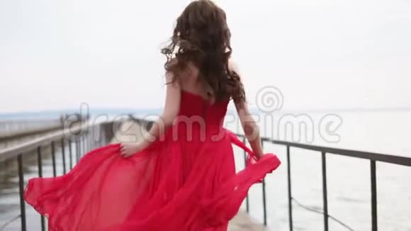 浪漫的年轻女孩穿着红色的裙子在古老的木海码头上奔跑视频的预览图