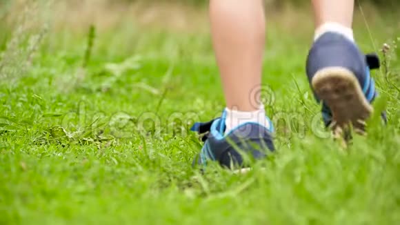 一个穿运动鞋的孩子的腿在绿草上特写视频的预览图