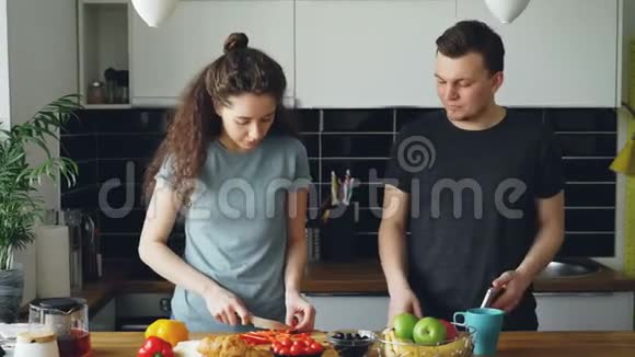 积极的年轻白种人夫妇在智能手机上听音乐跳舞女人切红胡椒并给她尝试视频的预览图