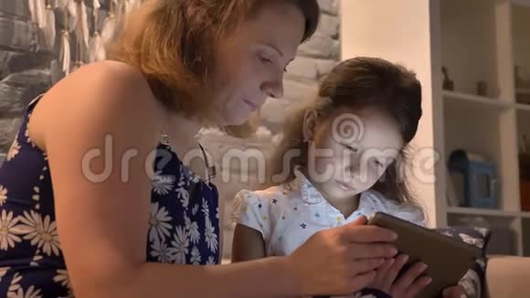 母亲带着小女儿使用平板电脑坐在现代家庭的沙发上家庭概念和小玩意在室内视频的预览图