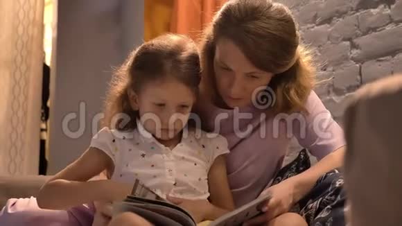 妈妈给小可爱的女儿读书一起坐在现代客厅家庭观念室内视频的预览图