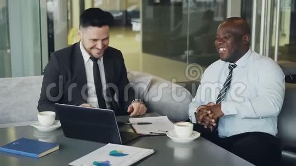 两个多民族商人看着笔记本电脑在玻璃咖啡馆笑非裔美国商人视频的预览图