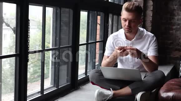一个年轻人坐在窗台上用笔记本电脑和智能手机工作视频的预览图
