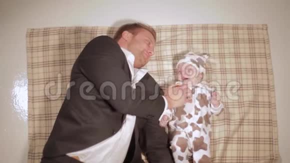 穿着西装的年轻白种人躺在棕色毯子上玩着尖叫的婴儿视频的预览图