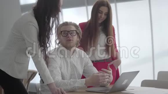 戴眼镜的金发男人坐在一间舒适的办公室里桌上放着上网本向同事们解释他的想法视频的预览图