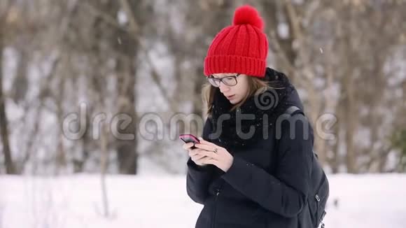 情绪化的年轻女孩带着眼镜和一顶红色针织帽子在手机上和一个男人说话高加索女人用粉色视频的预览图