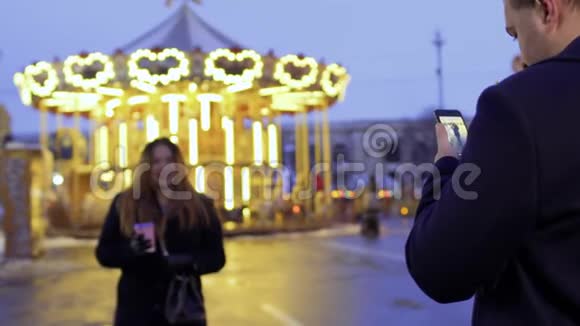 丈夫在旋转木马背景上用手机拍妻子的照片视频的预览图