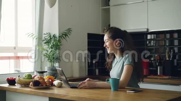 一位年轻的卷曲的非常积极的高加索女人坐在桌子旁在笔记本电脑上打视频电话视频的预览图