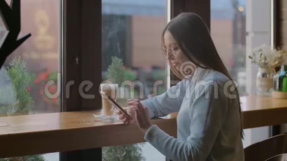 漂亮的女人在咖啡馆的智能手机上使用应用程序视频的预览图